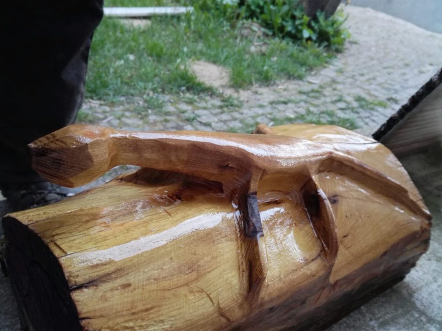 Holzskulptur eines stilisierten Tieres auf einem Baumstamm, glänzend und naturbelassen.